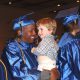 This photo shows a smiling male graduate holding a child