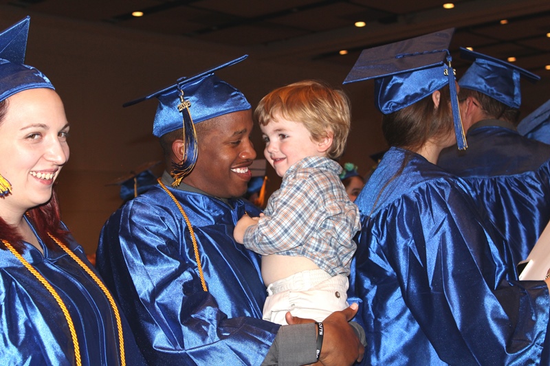 This photo shows a smiling male graduate holding a child
