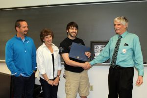 This photo shows a smiling student receiving an award from faculty members