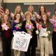 This photo shows a group of smiling females holding socks for the Sock It To Cancer fundraiser