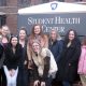 This photo shows a group of females smiling in front of the Student Health Center at Penn State