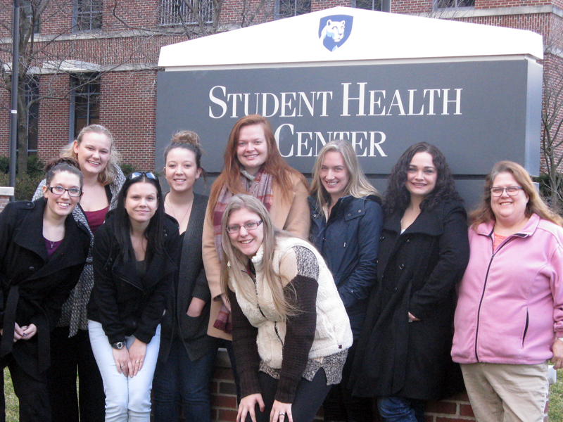 This photo shows a group of females smiling in front of the Student Health Center at Penn State