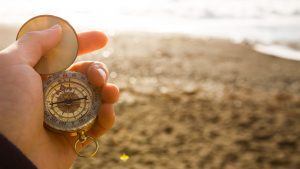 Point of view photo of man holding compass in the hand on the sea and beach background.